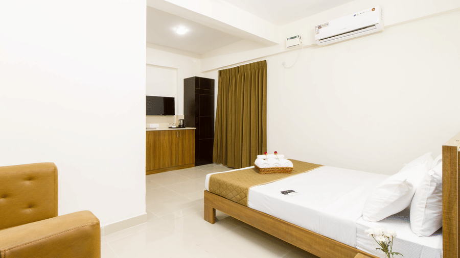 Hotel room with a single bed, a sofa, an air conditioner, and floor-length wooden curtains at Sanctum Suites Whitefield, Bangalore.