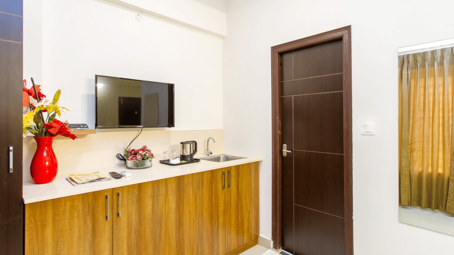 Hotel room with a television, wooden dresser, bamboo panel wall, and a red floral vase at Sanctum Suites Whitefield, Bangalore.