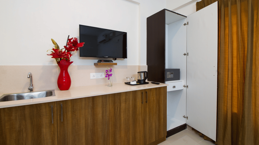 Hotel room with a wall-mounted television, a wooden dresser, and a red floral vase accent at Sanctum Suites Whitefield, Bangalore.