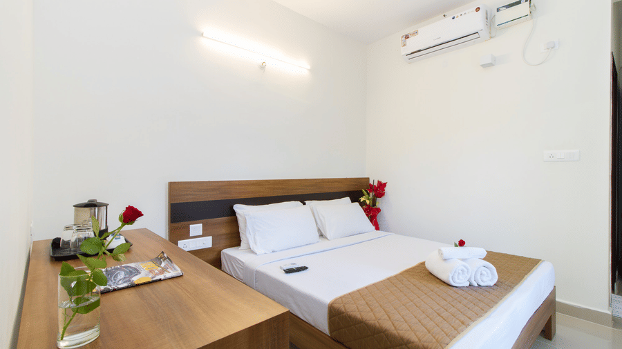 Hotel room with twin beds, white linen, wooden headboards, and an air conditioner at Sanctum Suites Whitefield, Bangalore.