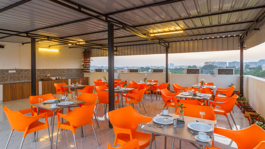 Open-air rooftop dining terrace with orange seating, pergola shading, and panoramic city views at Sanctum Suites Whitefield, Bangalore.