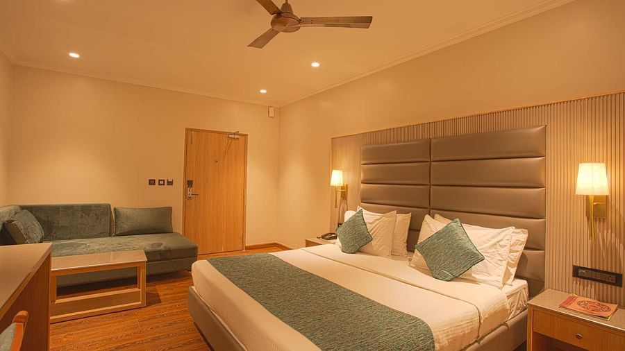 a double bed with a ceiling fan and lounger on the side inside Pool view room - The Cindrella Hotel, Siliguri