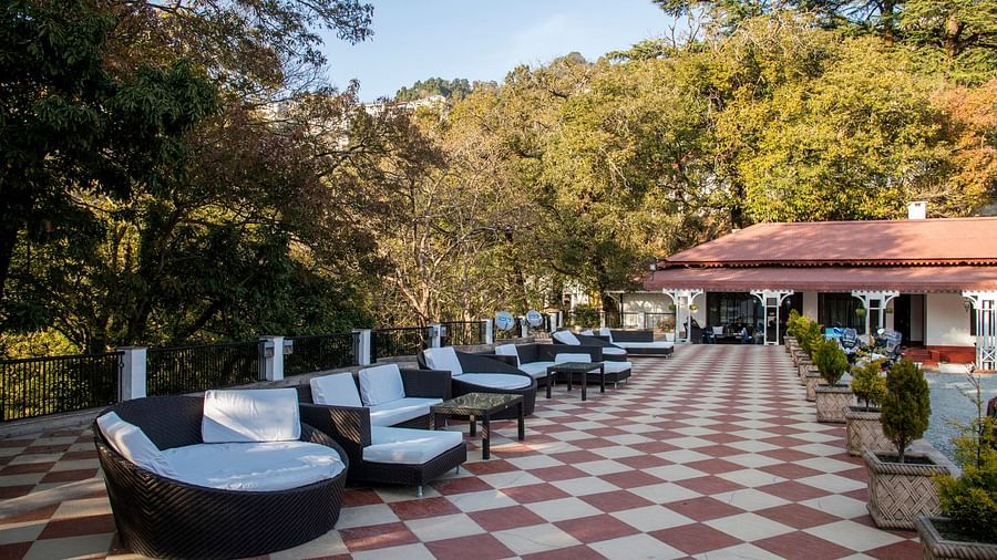 An outdoor seating area at The Claridges Nabha Residence in Mussoorie, characterized by comfortable, plush seating and encircled by a dense, lush green forest.