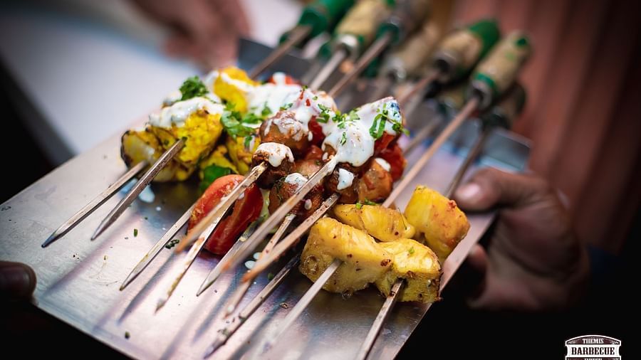 A plate of assorted grilled skewers with a variety of marinades and garnishes held by someone at Themis Barbecue House, Ambience Mall, Gurugram