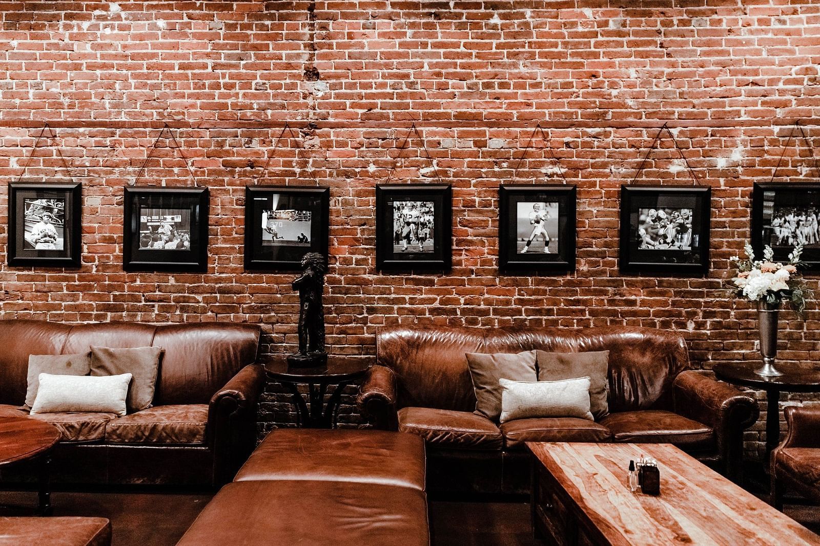 Sitting arena with brown sofas and wooden tables accompanied by brick textured wall with hanging wall art in the background 