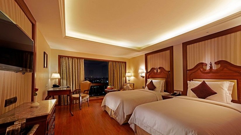 Room with cosy twin beds and expansive window offering the view of the city at Hablis Hotel, Chennai