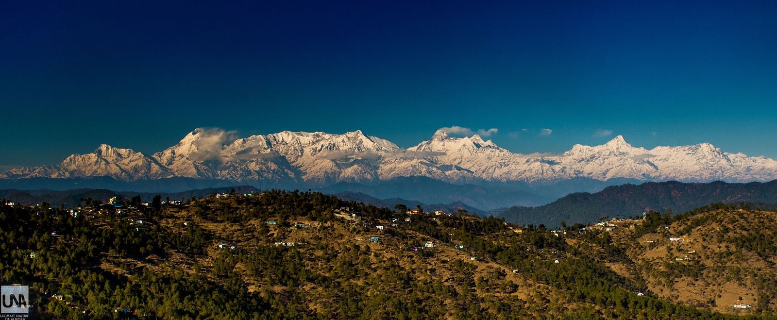 Scenic views of the Himalayas surrounded by lush greenery and set against the backdrop of rolling hills and blue skies.