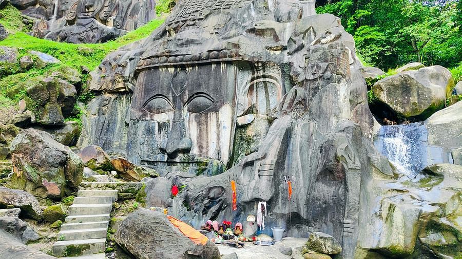 Ancient rock carvings of Buddha's face on a cliffside, surrounded by natural greenery and steps leading to the site.