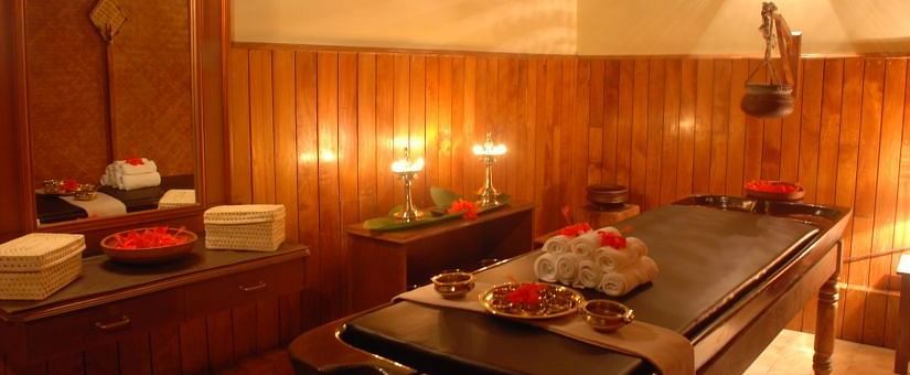 Warmly lit spa treatment room with a massage table and various wellness products - BluSalzz Collection - Tranquil Resort, Wayanad