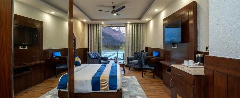  A spacious hotel room with a comfortable bed, a seating area, and a view of the mountains | DLS La Serene Manali