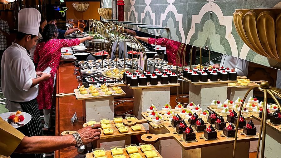 Dessert buffet at a restaurant with an array of sweet treats including cakes, pastries, and fruit desserts, presented on wooden and golden serveware under warm ambient lighting.