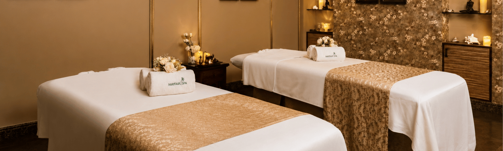 Spa treatment room with two massage beds, folded towels, framed paintings, candles and niche shelving at MAYFAIR Palm Beach Resort, Gopalpur-on-Sea.