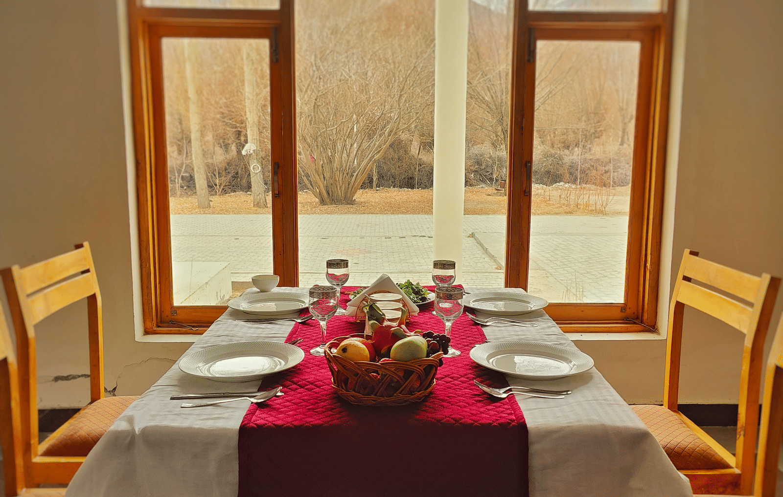A wooden dining table for four set neatly in front of a large window with a scenic view at Indus Serenity Retreat.