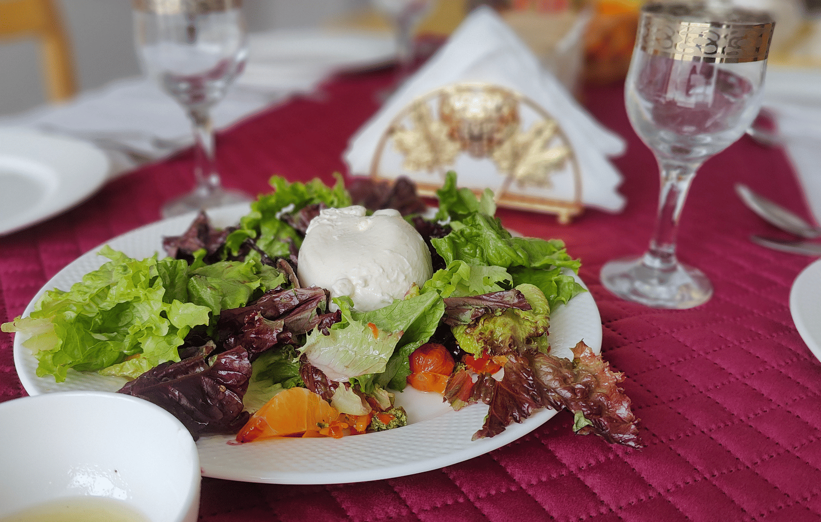A close-up of a fresh green salad served on a white plate over a textured red table runner at Indus Serenity Retreat.