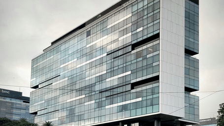 A modern glass-fronted building rises elegantly, reflecting the surrounding skyline beneath an overcast sky.