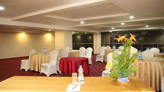 Empty chairs facing the stage alongside tables covered in decorative clothes, beside a rectangular table with a flower vase on top - Monarch Hotels