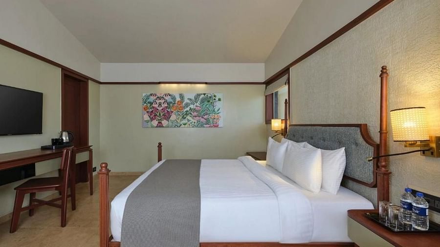 Side view of a double bed with grey bedsheet, a chair  a small side table and a beautiful painting on the wall at Pride Resort Ambaji