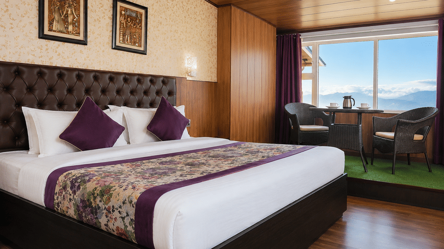 Attic Room at Valmere Thistle Boutique Hotel, Darjeeling with a king bed, an elevated seating nook, and a window overlooking distant mountains.