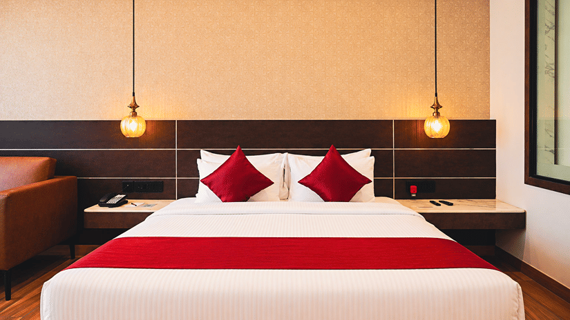 Spacious king-bedded guest room with warm lighting, wooden flooring and modern interiors at HM Hotel & Resort, Dibrugarh, offering a comfortable stay in Assam