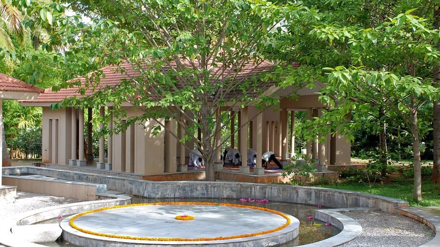 A circular feature surrounded by trees and a building with a thatched roof, outdoor setting - Shreyas Retreat