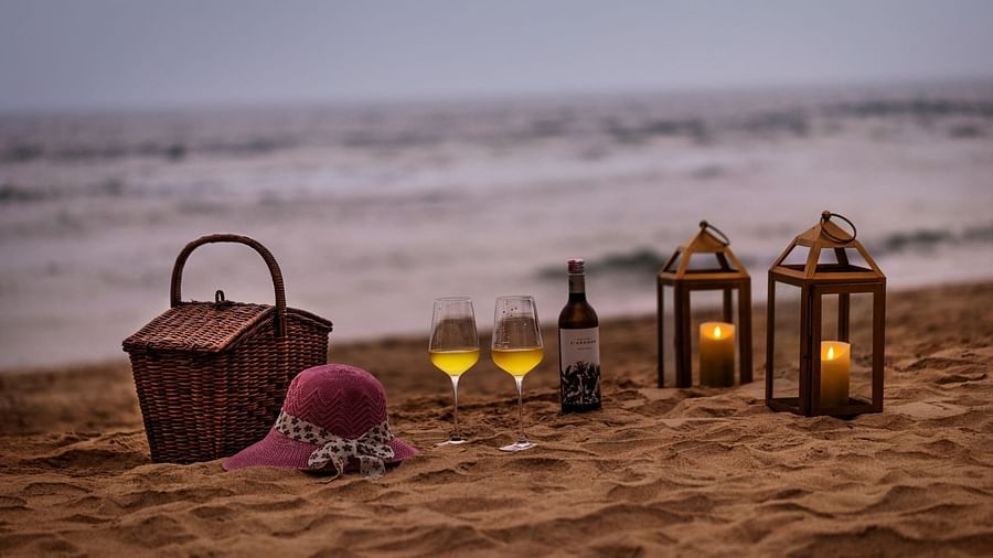  A romantic beach setup with a picnic basket, wine glasses, lanterns, and a hat against the serene backdrop of waves - Heritage Village Resorts & Spa, Goa