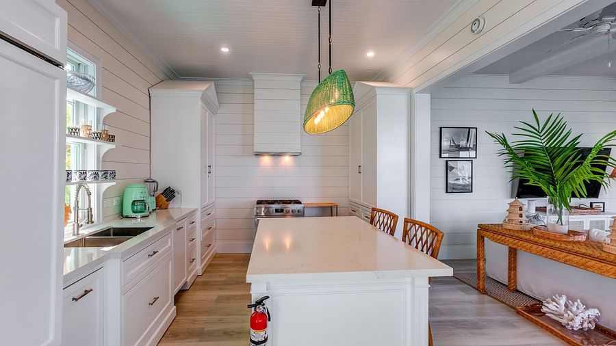 Modern kitchen with white cabinetry, wooden stools, and green pendant light | Abaco Inn