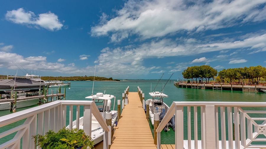 Boardwalk extending over water with white railings, leading to a dock with boats | Abaco Inn