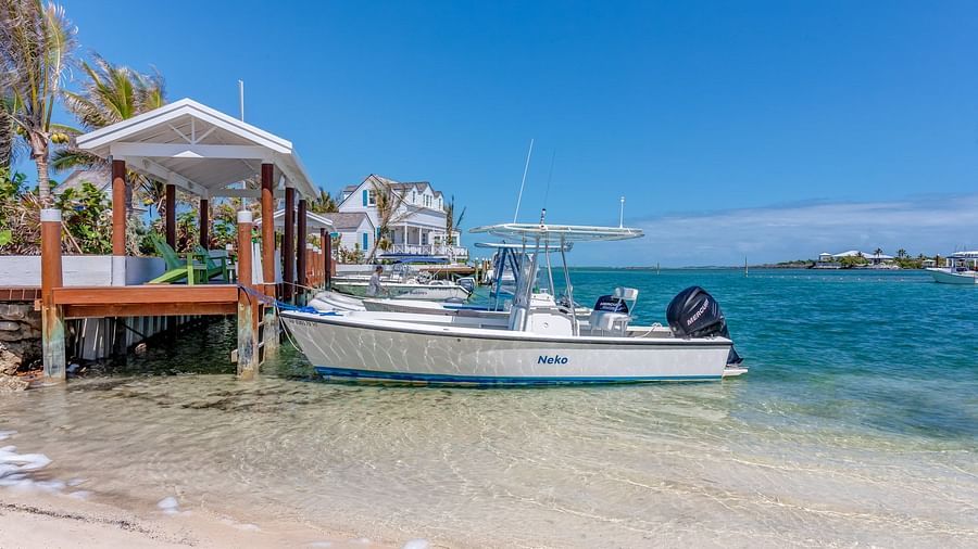 Boat docked at a shore with houses and palm trees | Abaco Inn