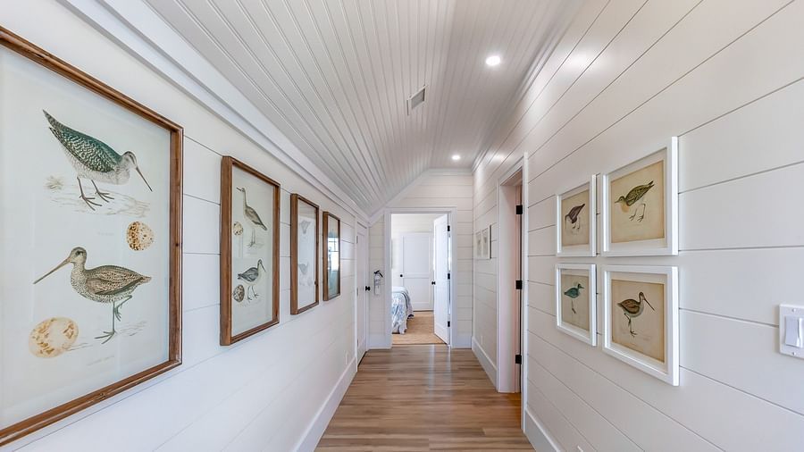 a corridor with wooden floor and white walls with paintings at Abaco Inn.