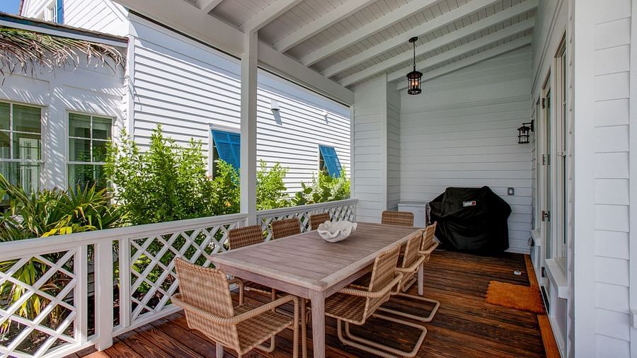 A spacious outdoor porch with a dining table and chairs, a grill, and a railing, offering a view of nearby structures - Abaco Inn