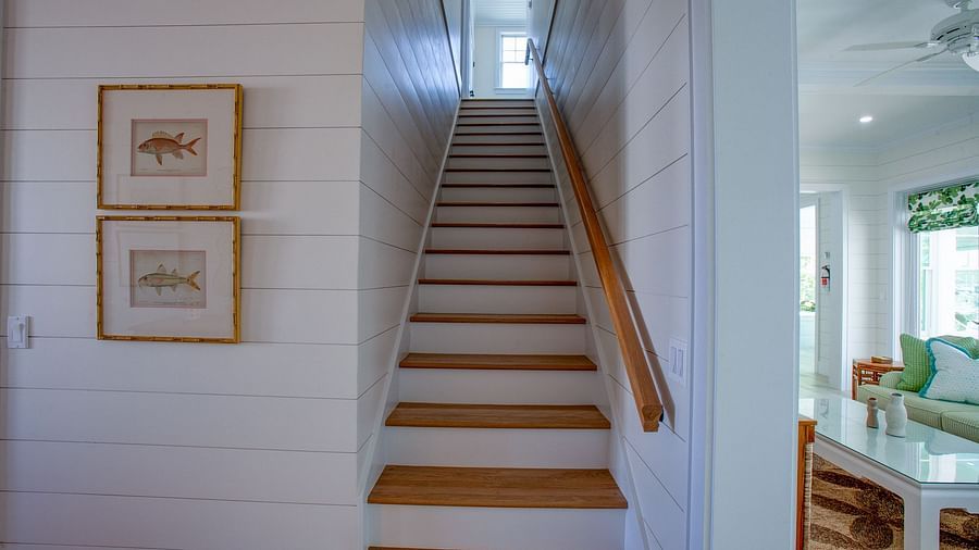 An indoor staircase with wooden treads and risers, featuring framed artworks on the adjacent wall, leading upwards and out of view - Abaco Inn