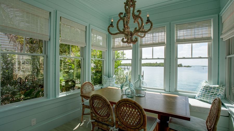 An elegant dining area with a large, ornate chandelier suspended above a wooden table surrounded by chairs, set within a room with numerous windows - Abaco Inn