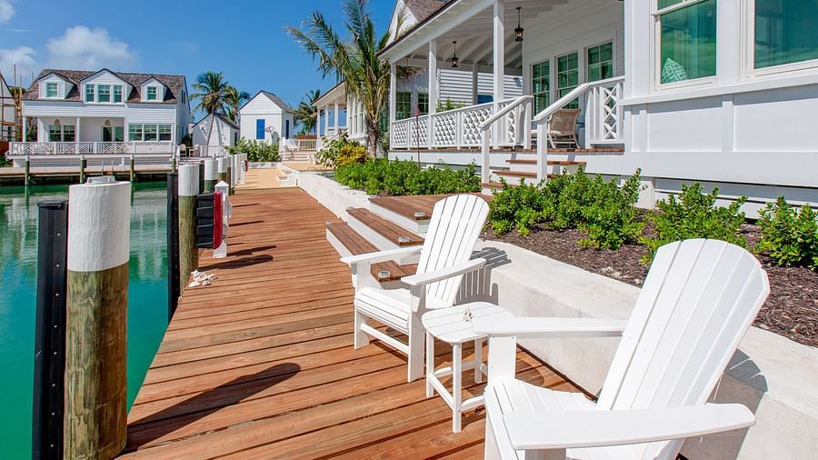 A wooden pier extending over water, with a set of lounge chairs and views of a cluster of waterfront houses under a bright sky - Abaco Inn