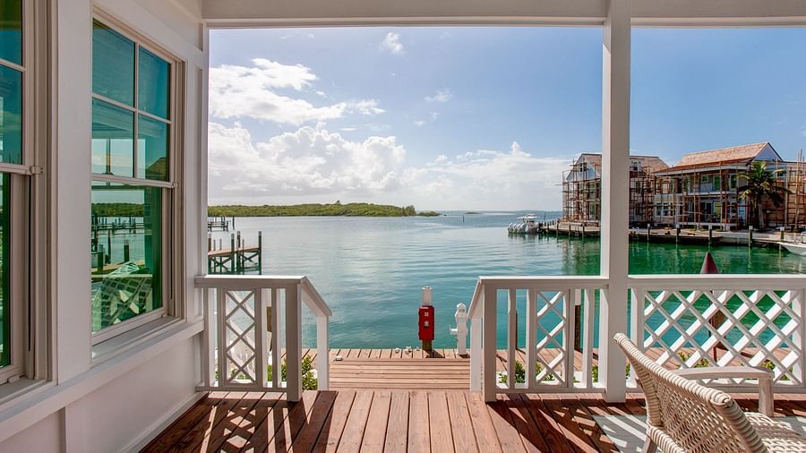 A waterfront porch featuring a wooden deck and railing, overlooking a body of water with distant buildings under a clear sky - Abaco Inn