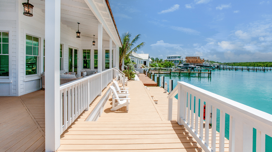 A wooden balcony walkway at Shoal Villa in Abaco Inn with white railings, outdoor seating, ceiling fans, and open water views.