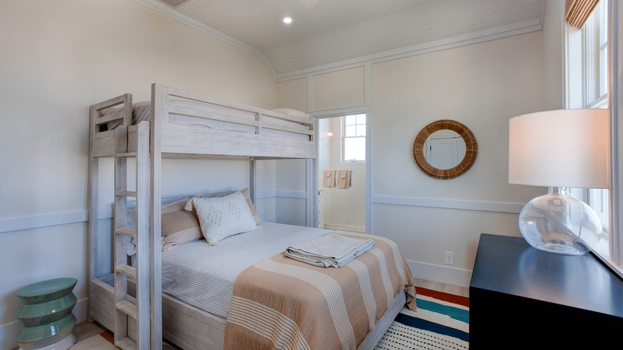 A bedroom at Shoal Villa in Abaco Inn featuring a wooden bunk bed, neatly arranged bedding, a side table, a table lamp, and a decorative mirror.