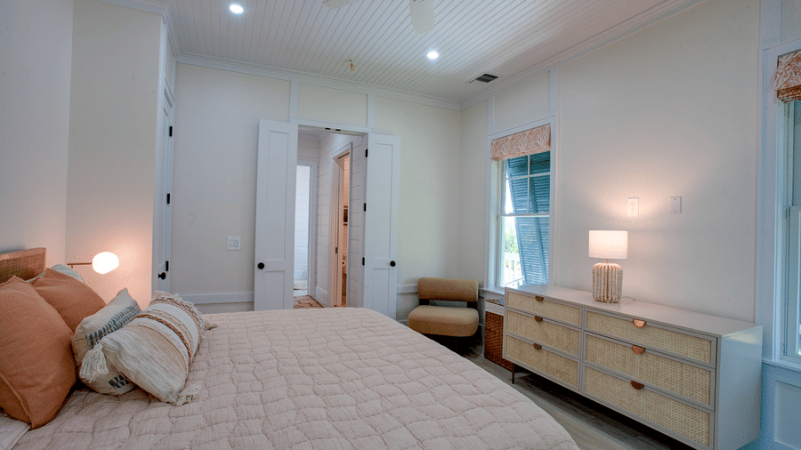 A master bedroom of Shoal Time Villa at Abaco Inn with a neatly made bed, bedside lamps, ceiling fan, dresser, and an open doorway leading to another room.