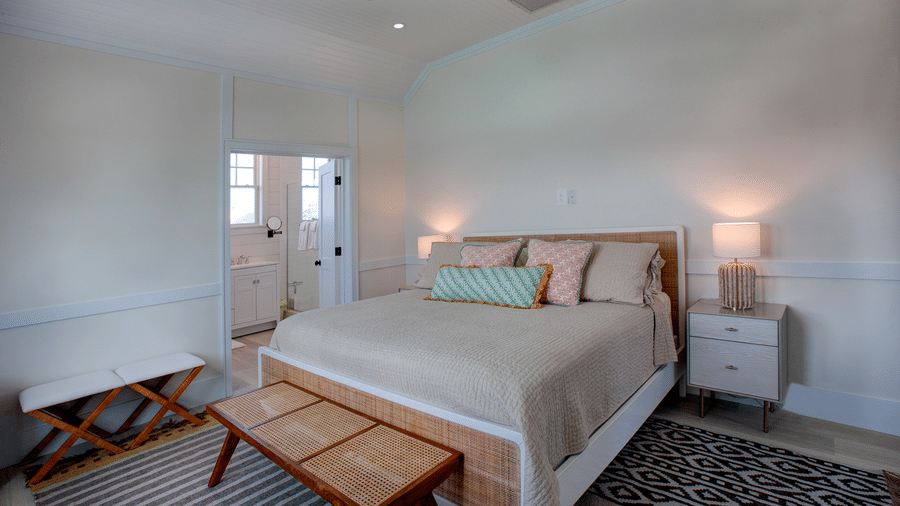 A bedroom interior at Shoal Villa in Abaco Inn with a double bed, bedside tables, table lamps, a patterned rug, and a bench at the foot of the bed.