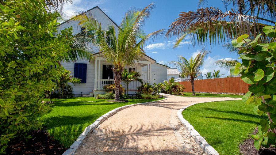 A landscaped garden pathway at Shoal Villa in Abaco Inn with manicured lawns, palm trees, shrubs, and resort buildings visible ahead.