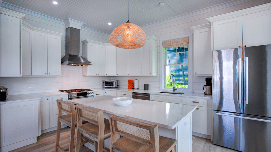 A kitchen at Shoal Villa in Abaco Inn with a central island, bar stools, built-in cabinets, pendant lighting, and stainless steel appliances.