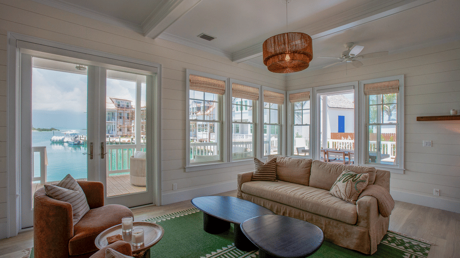 A living room at Shoal Villa in Abaco Inn with sofas, armchairs, a coffee table, large windows on multiple sides, and a ceiling light fixture.