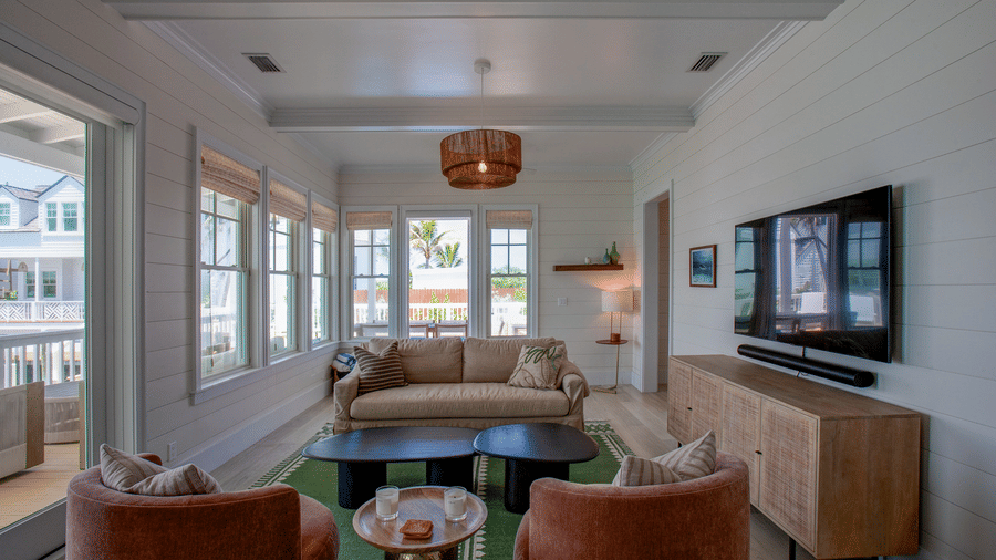 A living room at Shoal Villa in Abaco Inn with sofas, armchairs, a coffee table, wall-mounted television, large windows, and ambient lighting.
