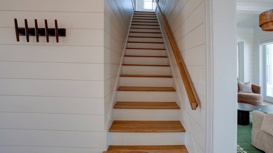 An indoor staircase at Shoal Villa in Abaco Inn with wooden steps, white walls, a handrail, and wall-mounted decor..
