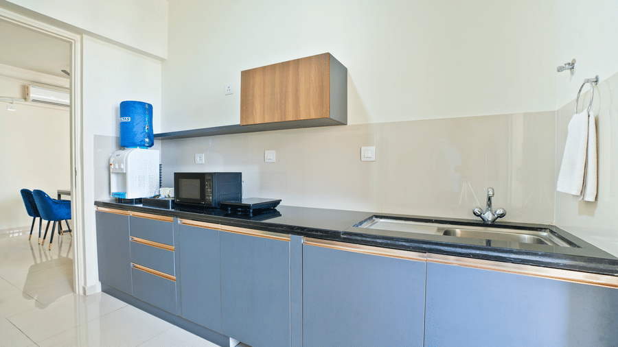 A compact, modern kitchenette in a studio apartment featuring grey cabinets, a black countertop, a microwave, and a water cooler at Apartel by Aarin, Oragadam.