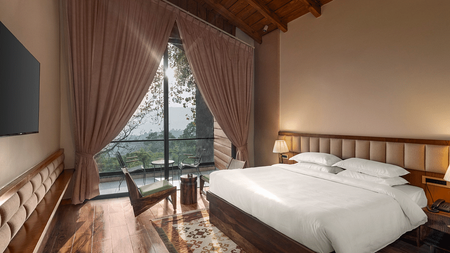 A cosy bedroom with a wooden floor and ceiling, large draped window with a scenic view, and a comfortable sitting area - The Samai, Bhimtal