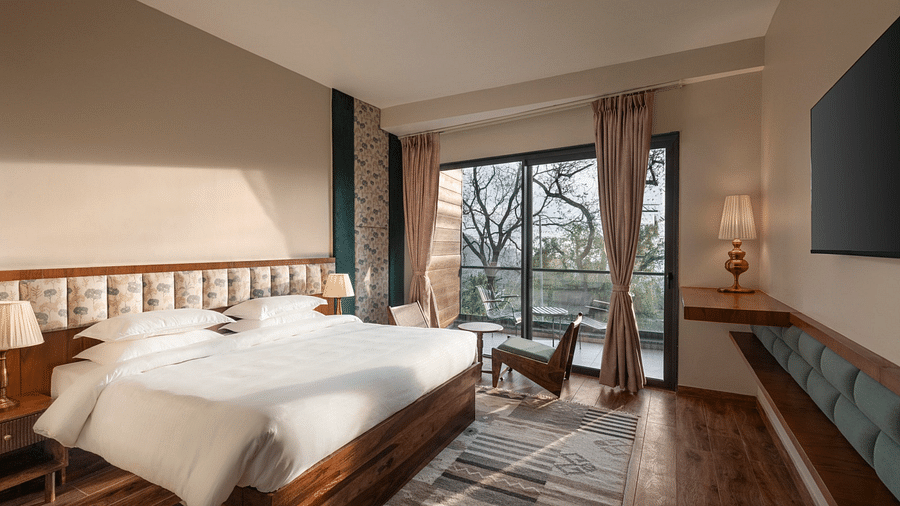 A spacious room decorated with a floral pattern headboard, large windows overlooking greenery, and contemporary furniture - The Samai, Bhimtal