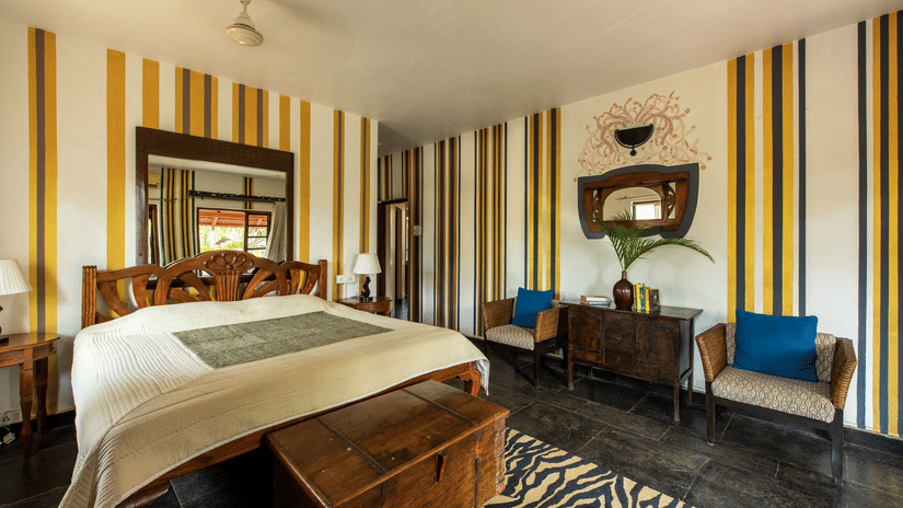 Spacious bedroom with a king size bed, striped walls, wooden furnishings and blue accent chairs.