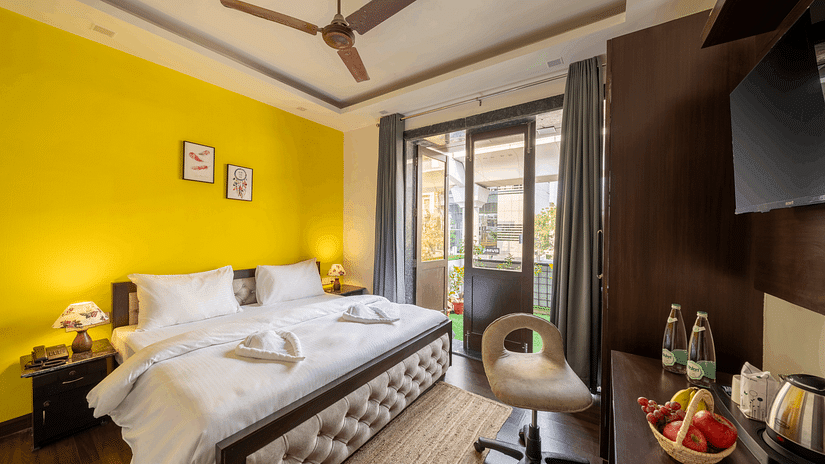 An image of a bedroom featuring a double size bed, a chair, a flat TV screen, a table with fruit basket and tea and coffee maker, and  a glass door leading to the balcony - Lime Boutique Bed & Breakfast, Nehru Place Metro