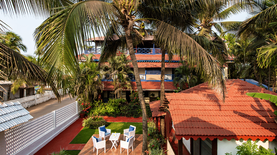 Elevated view of red-roofed cottages, palm trees, garden seating and a swimming pool.