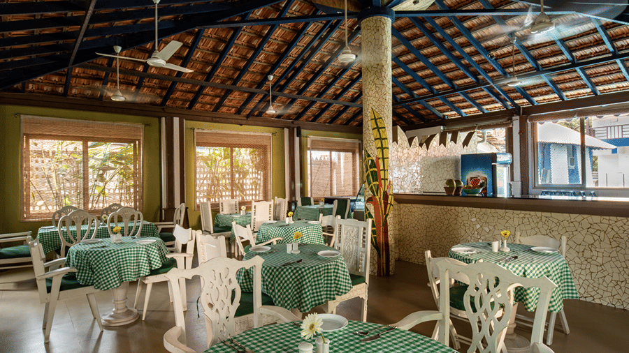 Covered dining area with green checked tablecloths, white chairs and tables beneath a traditional tiled roof.